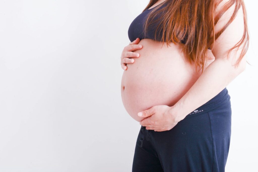 Mulher grávida acariciando a barriga com as duas mãos.