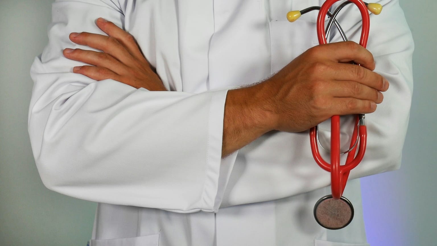 Médico da família com braços cruzados segurando estetoscópio, representando confiança e cuidado integral.